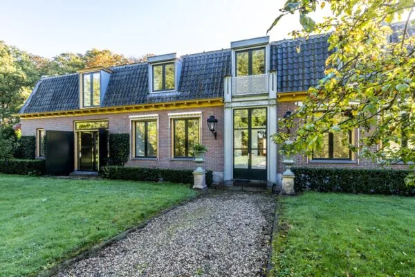 Vooraanzicht van een statige woning aan de Langbroekerdijk met grote ramen, donkere dakpannen en een grindpad naar de entree.